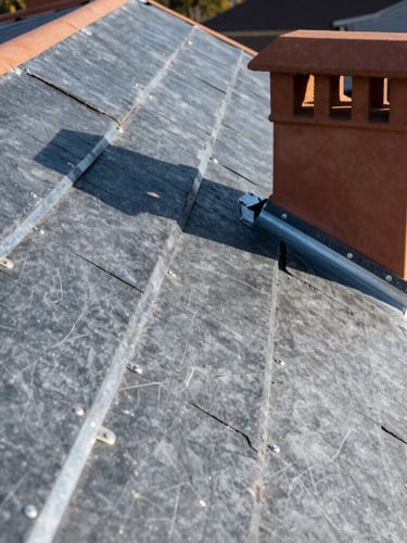 High-angle editorial construction photography of a newly laid zinc and slate roof, crisp morning daylight highlighting metallic joints, warm terracotta chimney details, sharp focus, 35mm