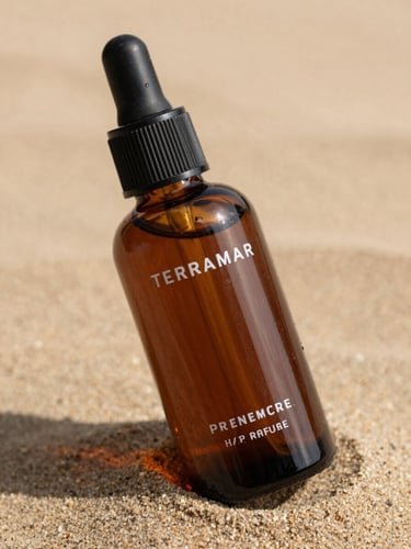 Close-up macro shot of Terramar premium hair oil bottle on a warm sand background with soft daylight shadows