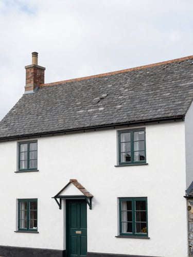 Medium shot of a traditional Devon slate-roof cottage exterior in bright overcast daylight, clean architectural photography, 35mm lens.