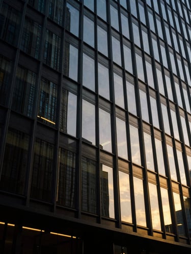 Low-angle architectural shot of a modern steel-and-glass skyscraper facade reflecting twilight golden hour light, deep obsidian tones