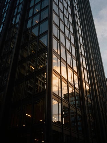 Low-angle dramatic architectural shot of a modern glass skyscraper reflecting twilight sky, sharp gold accents, deep shadows, 35mm film aesthetic