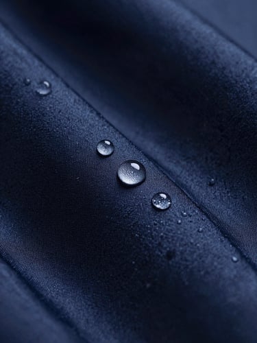 Macro studio shot of water droplets perfectly spherical, beading on raw silk fabric under soft dramatic side lighting, deep navy background.