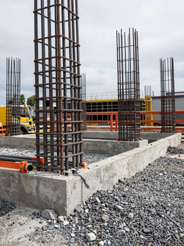 Heavy concrete foundation being poured around steel reinforcement rebars on an industrial jobsite, overcast daylight, gritty texture