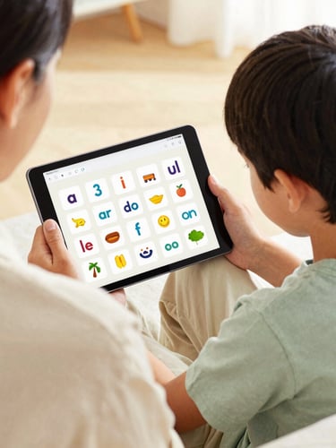 Over-the-shoulder view of a parent sitting supportively next to a focused boy looking at a tablet screen showing interactive French phonics cards, warm editorial photography, soft natural daylight.