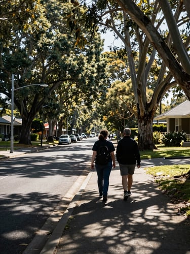 Wide shot of a tree-lined Melbourne suburban street at mid-morning, a support worker walking beside a participant on the footpath, shot from behind at distance, dappled natural light through eucalyptus canopy, no faces visible, candid and unhurried