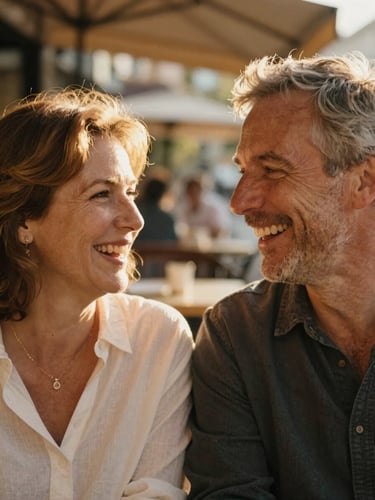 Close-up of a mature couple laughing together in warm golden-hour light, soft focus, authentic French cafe terrace in the background.