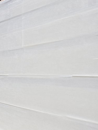 A close-up shot of an EIFS certified professional applying a smooth base coat over a clean moisture barrier mesh, bright daylight, realistic texture.