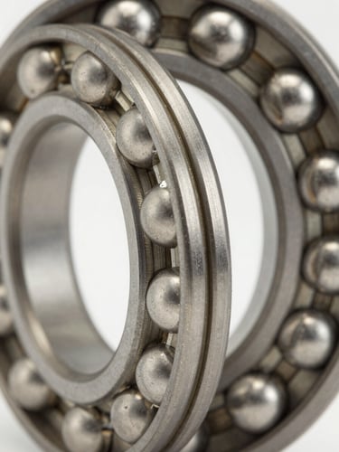Extreme close-up of a steel ball bearing race, balls and inner ring filling the frame, bright even studio lighting revealing machined groove geometry and polished metal surfaces, sharp focus on the bearing contact track