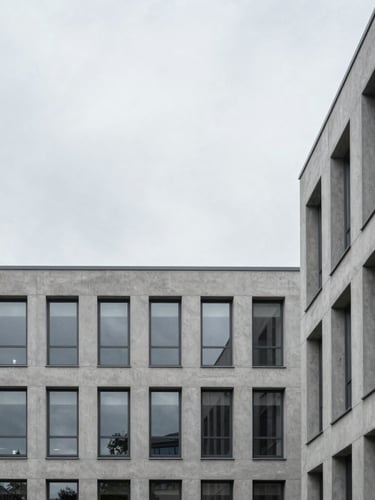 Minimalist modern office building in Northern Germany with clean concrete lines, overcast grey sky, desaturated tones, architectural crop.