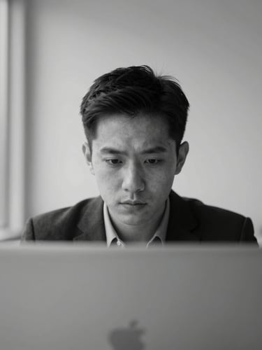 Close-up portrait of a focused professional in a minimalist grey workspace, sharp natural light, high-contrast monochrome style.