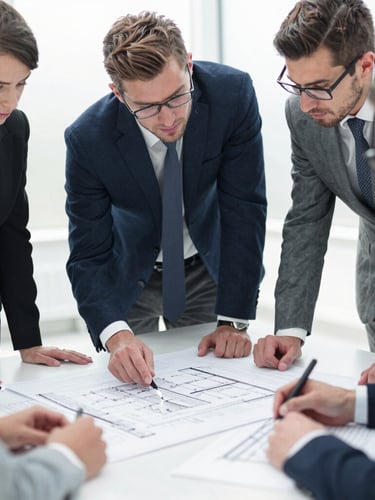 Professional team members in an active strategy session, reviewing blueprints on a large table, bright natural daylight, deep navy and cool gray tones, sharp focus, 35mm