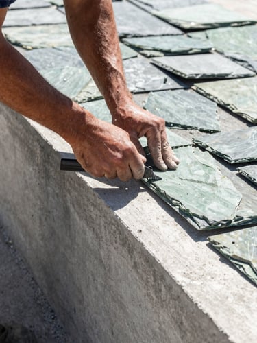Close-up of a professional masonry team member hand-carving slate textures onto a freshly extruded concrete border, bright morning light