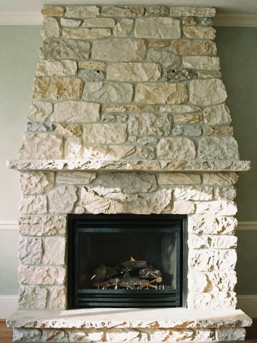 A warm editorial photograph of a sunlit stone fireplace in a Laurentian estate, soft natural daylight, muted forest green and cream tones, shallow depth of field, 35mm.