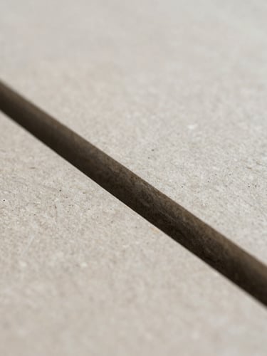 Tight abstract close-up of high-quality architectural materials, textured stone and dark metal lines in soft diffused daylight, minimalist editorial photography