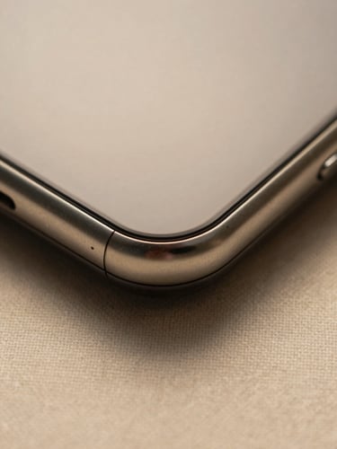 Extreme close-up overhead study of a Bravo phone's metal edge and speaker grille resting on a linen surface, warm tungsten studio light casting a short shadow, the machined chamfer in sharp focus, soft bokeh on the surrounding cloth