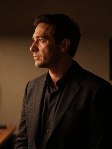 Moody low-key portrait of a creative director in a dark London studio, dramatic shadows, warm tungsten light highlighting the profile, professional, sophisticated.