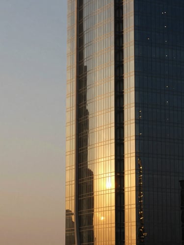 Architectural abstract of a modern luxury glass tower in Ras Al Khaimah, golden hour light reflecting off steel, clean lines, negative space on the left