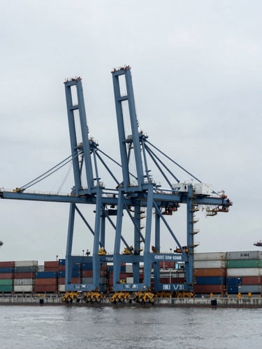 Wide-angle industrial photography of a modern shipping terminal, towering container cranes under heavy overcast daylight, desaturated blue and slate gray tones, sharp focus, 35mm.