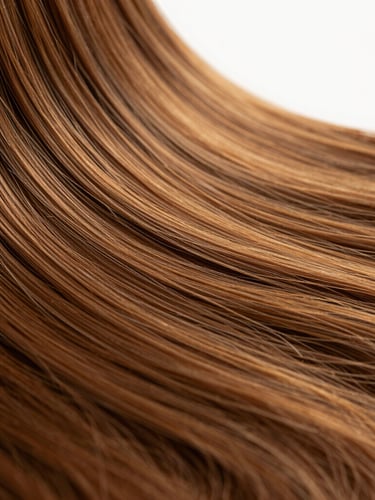Macro close-up of premium warm chestnut brown hair extensions, showing flawless silky texture and natural shine under soft studio backlighting, shallow depth of field