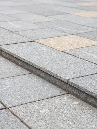 A close-up architectural shot of perfectly aligned gray stone pavers, showing crisp geometric joints and a level edge, bright overcast daylight, rich textures of premium materials.
