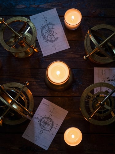 Overhead flat-lay of brass astrolabes and hand-drawn birth charts on a dark wooden table, low-key warm candlelight, rich amber tones