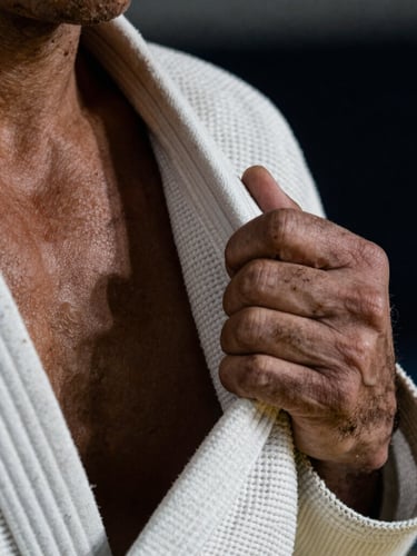 A close-up macro photograph of a tightly gripped white gi lapel by a weathered hand, dramatic high-contrast side lighting, gritty athletic texture, 35mm lens.