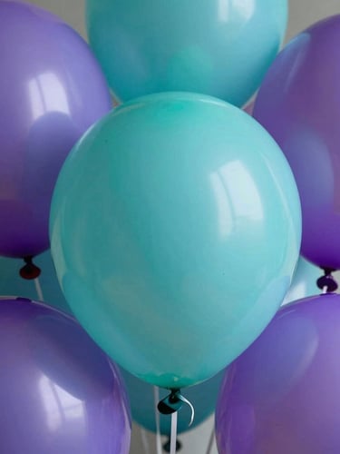 Macro shot of high-grade latex balloons showing rich matte textures and vibrant turquoise and purple colors under soft studio lighting.