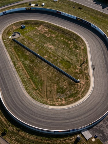 Dramatic top-down aerial of the Traction Motodrome track geometry, sharp corners and wide run-off zones visible under harsh sunlight.