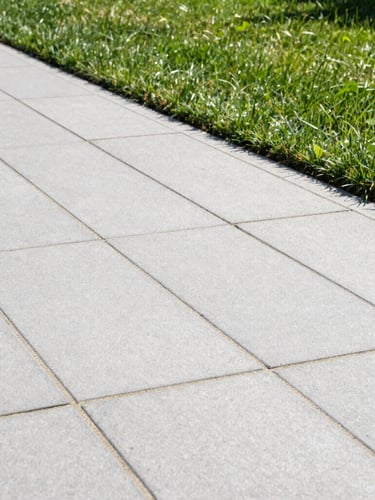 A crisp, level paver walkway with tight, clean sand joints, bordered by freshly cut green lawn under bright midday sun, showing clean straight edges.