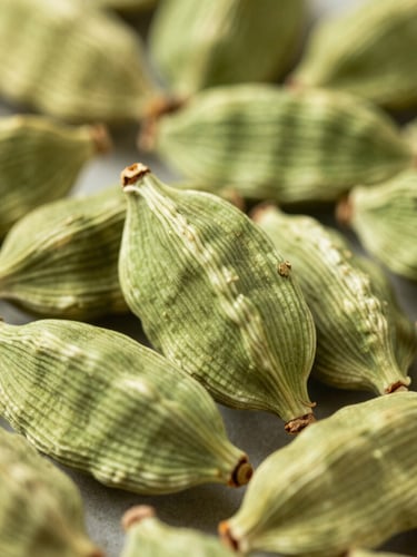 Macro overhead shot of raw green cardamom pods in bright natural daylight, rich saturated green and turmeric tones, sharp focus, shallow depth of field