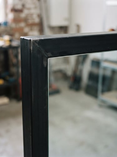 Macro photograph of a seamless black steel frame corner meeting clean glass, minimalist interior, soft morning light, industrial-minimalist, 35mm