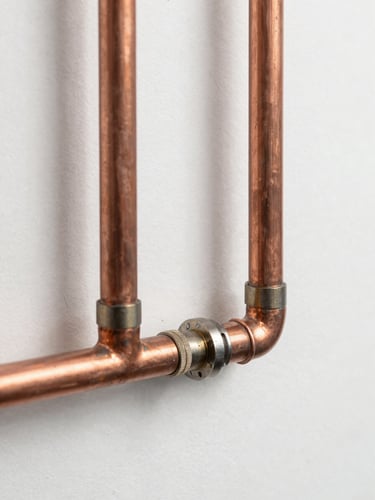 A clean, newly installed copper pipe system on a white wall, showing precise solder joints, bright daylight, sharp macro focus, technical engineering style.