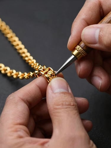Close-up of a master craftsman hands using traditional hand tools to finish an intricate gold necklace, warm gold reflections, macro lens, shallow depth of field