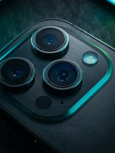 Sharp close-up of a smartphone camera lens module with cyan and green rim lighting on a dark metallic surface, 50mm macro lens