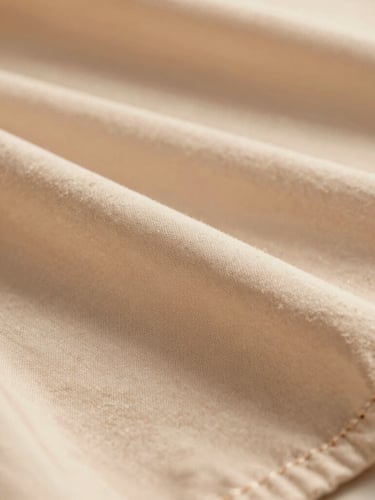 warm editorial fashion photography close-up of premium fabric texture with delicate stitching, warm golden-hour natural light, soft sand tones, shallow depth of field, 35mm