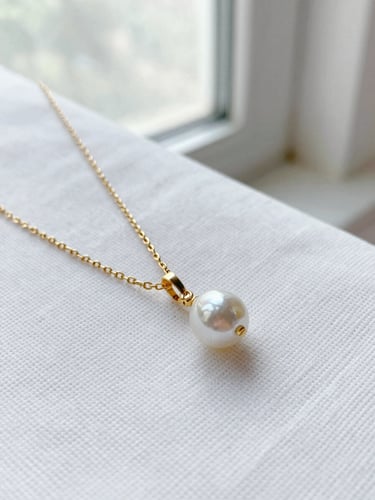 Macro shot of a delicate gold chain and pearl pendant resting on textured white linen, soft morning window light, shallow depth of field