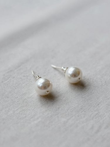 Still-life composition of silver earrings resting on textured light gray linen, soft overcast daylight, shallow depth of field.