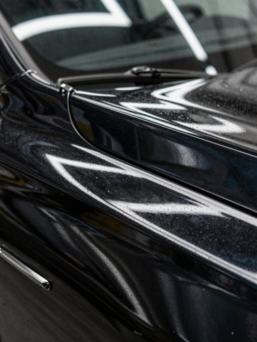 Extreme close-up of a flawless, mirror-like metallic black car body panel, reflecting sharp linear white LED strip lights from a workshop ceiling, absolute reflection clarity.