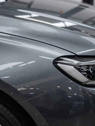A close-up macro shot of a luxury car fender showing a razor-sharp reflection of linear overhead LED strip lights, highlighting a flawless metallic dark grey paint finish with no imperfections.