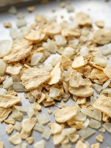 Macro commercial photography of premium dehydrated garlic flakes and white onion kibbles on a clean, industrial stainless steel surface, bright natural daylight, sharp focus