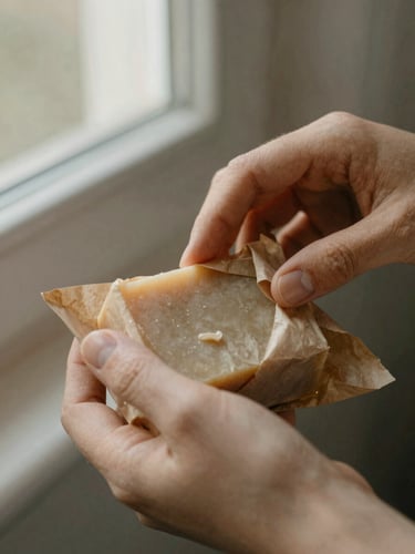 Close-up of hands gently wrapping a solid shampoo bar in biodegradable brown paper, soft afternoon window light, earthy muted tones