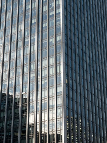 Vista de gran angular de un rascacielos corporativo moderno con paneles de vidrio y acero, iluminación diurna fría y sombras geométricas pronunciadas.