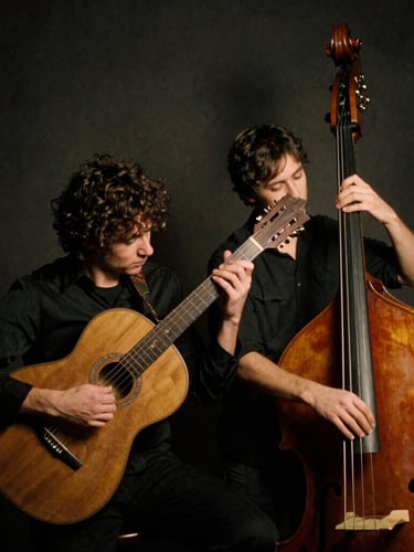Low-key atmospheric portrait of two musicians holding a vintage steel resonator guitar and upright bass, warm side lighting, dark charcoal background, 35mm film grain