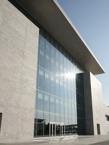 Sleek, modern architectural detail of the Dubai Airport Freezone, clean concrete facades, massive structural glass reflecting a clear sky, dramatic shadows, wide cinematic angle.