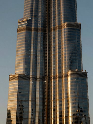 Cinematic portrait of a modern, towering glass skyscraper in Dubai during twilight, sharp contrast, deep shadows, golden light reflecting off the facade.