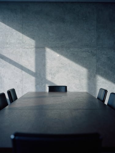 An empty high-end boardroom in Luxembourg City, soft natural northern light casting abstract geometric shadows on a concrete wall, minimalist composition