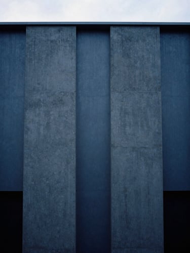 Minimalist architectural photography of a modern concrete and steel facade in Luxembourg, cool overcast daylight, deep blue and slate tones, sharp geometric shadows, medium format film composition