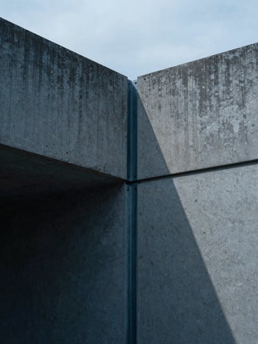 Extreme close-up of cast concrete textures and steel joints, sharp geometric shadows, cool northern European overcast daylight, minimalist architectural composition.