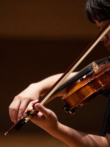 Intimate close-up of a young musician's hands holding a violin bow, soft side-lit rehearsal space, rich low-contrast shadows, shallow depth of field