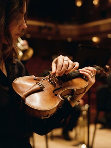 Intimate close-up of a young violinist's hands adjusting a wooden bridge, soft warm concert hall lighting, shallow depth of field, 35mm